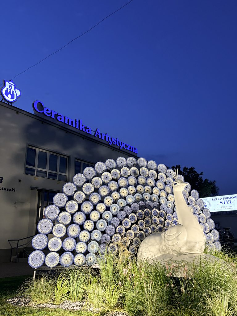 Podświetlona instalacja pawia z ceramicznym ogonem przed Ceramiką Artystyczną po zmroku